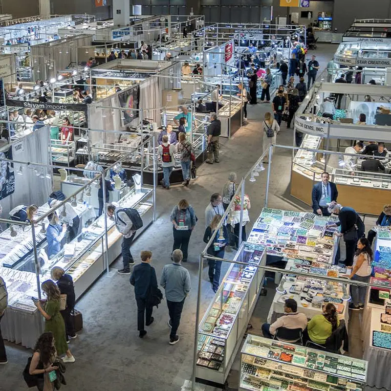 Wide view of the Tucson Gem & Mineral Shows trade floor with mineral and gemstone booths and display cases inside a convention hall.